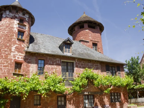 A majestic red sandstone manor with two towers and green vines in Collonges-la-Rouge, France.
