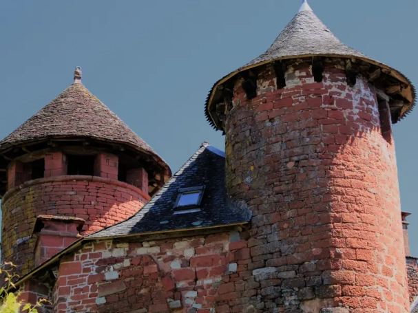 Iconic medieval red sandstone towers with slate roofs under a deep blue sky in Collonges-la-Rouge, France.