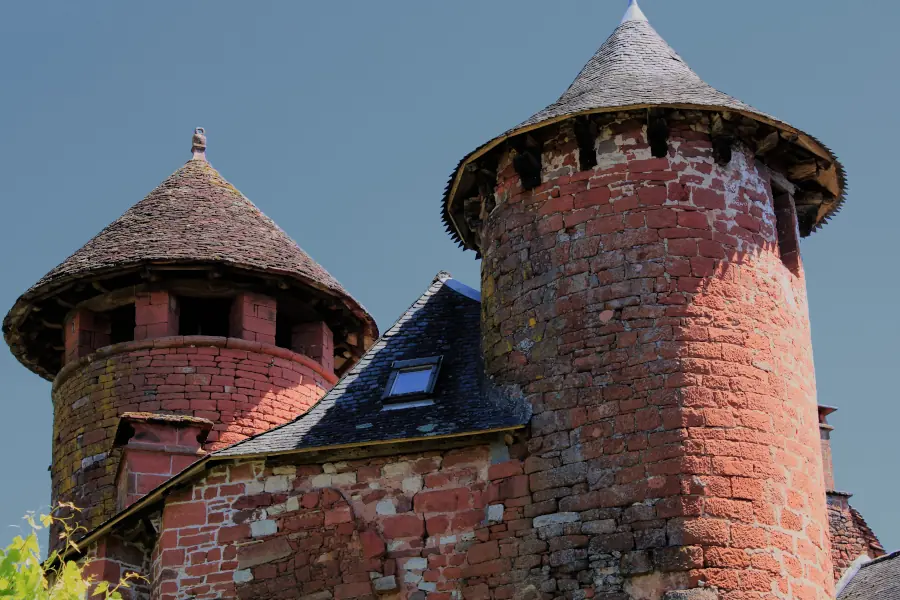 Iconic medieval red sandstone towers with slate roofs under a deep blue sky in Collonges-la-Rouge, France.