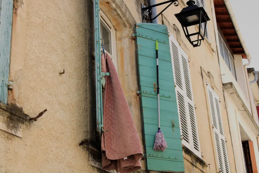 A rustic turquoise wooden shutter with a classic black iron lantern on a warm stucco facade in Tarascon, Provence.