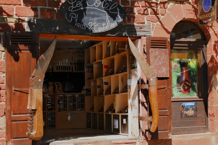 Giant wooden pocket knives used as window shutters on a traditional red sandstone knife shop in Collonges-la-Rouge, France.