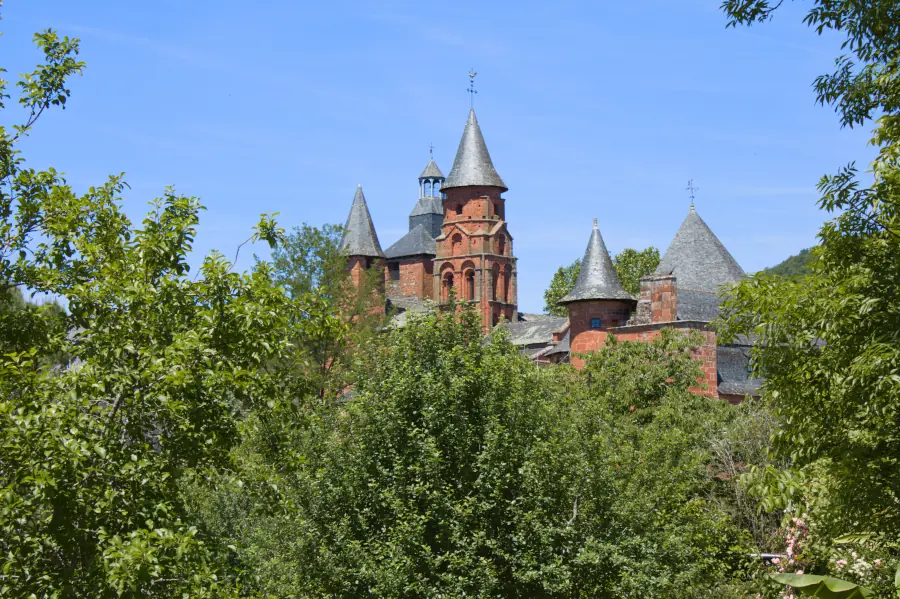 Red stone towers of Collonges-la-Rouge emerging from green trees under a blue sky.