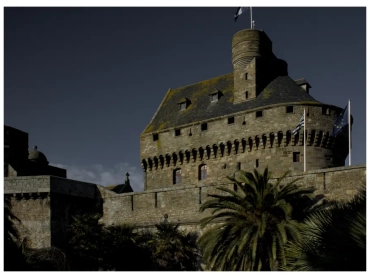 A fine art print of a medieval French castle displayed in a dark, atmospheric living room interior