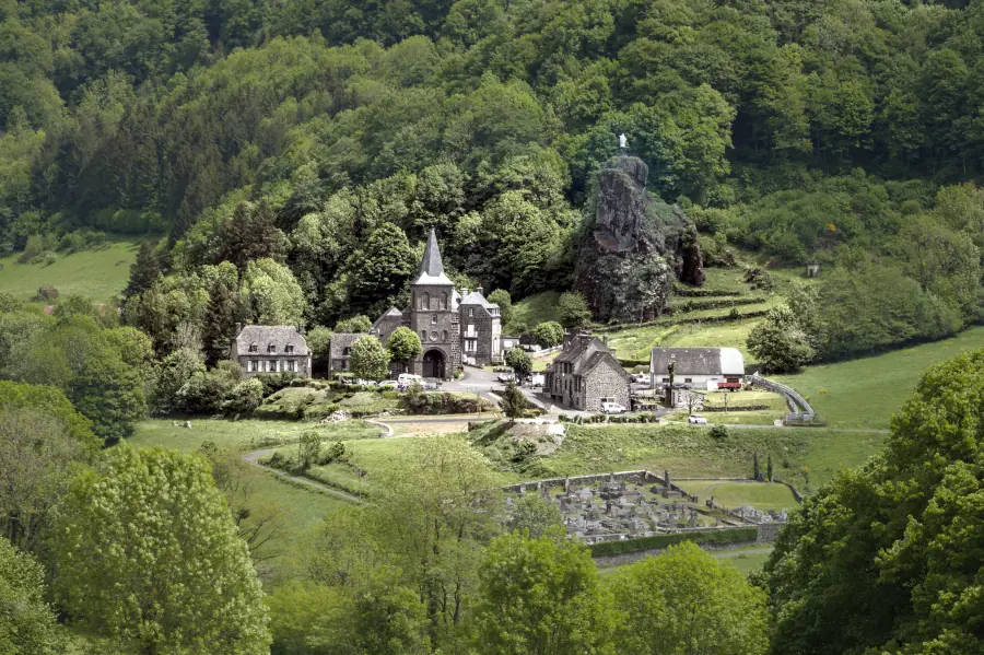 Panoramic view of Saint-Paul-de-Salers, Cantal, France, featuring the iconic volcanic rock and the Virgin Mary statue.