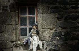 Witch doll sitting on a rustic stone window sill in the medieval village of Salers, France.