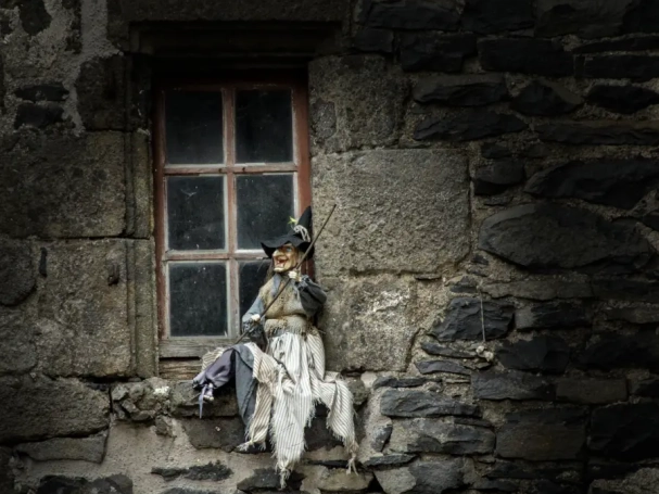 Witch doll sitting on a rustic stone window sill in the medieval village of Salers, France.